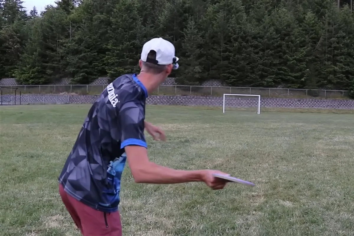 Gannon Buhr seen from behind reaching back low with a light purple disc held near hip height for a hyzer