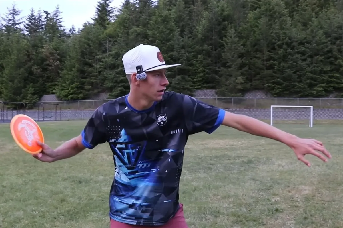 Gannon Buhr with his left arm stretched out in front of his body and an orange disc held back in his right hand